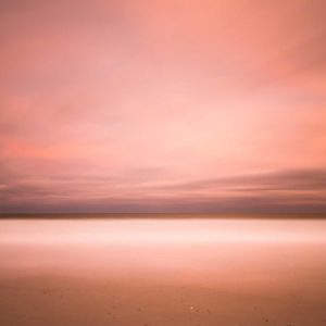 wide view of the ocean with beach in the foreground, orange sunset clouds creating an abstract view by the long exposure effect