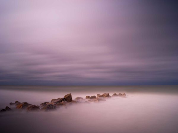 rocky groin with deep purple after sunset colors, an abstract view created by a long exposure photography technique
