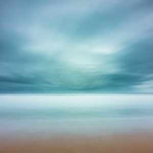 wide view of the ocean with beach in the foreground, blue strormy cloud cover creating an abstract view by the long exposure effect